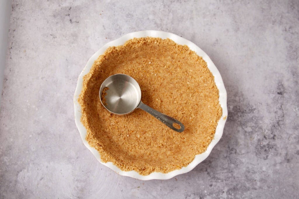 pretzel pie crust in a white pie dish with a metal measuring cup.