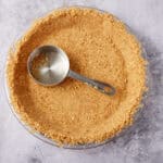 pretzel pie crust in a clear pie dish with a metal measuring cup.