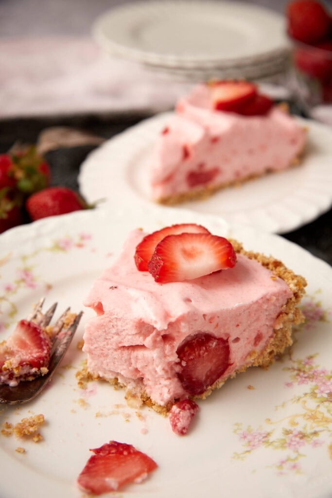 two slices of strawberry chiffon pie on with plates and one with a bite taken out of it. 