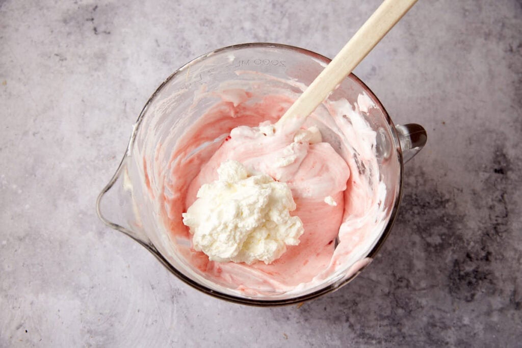 whipped cream being folded into the strawberry pie mixture with a spatula. 