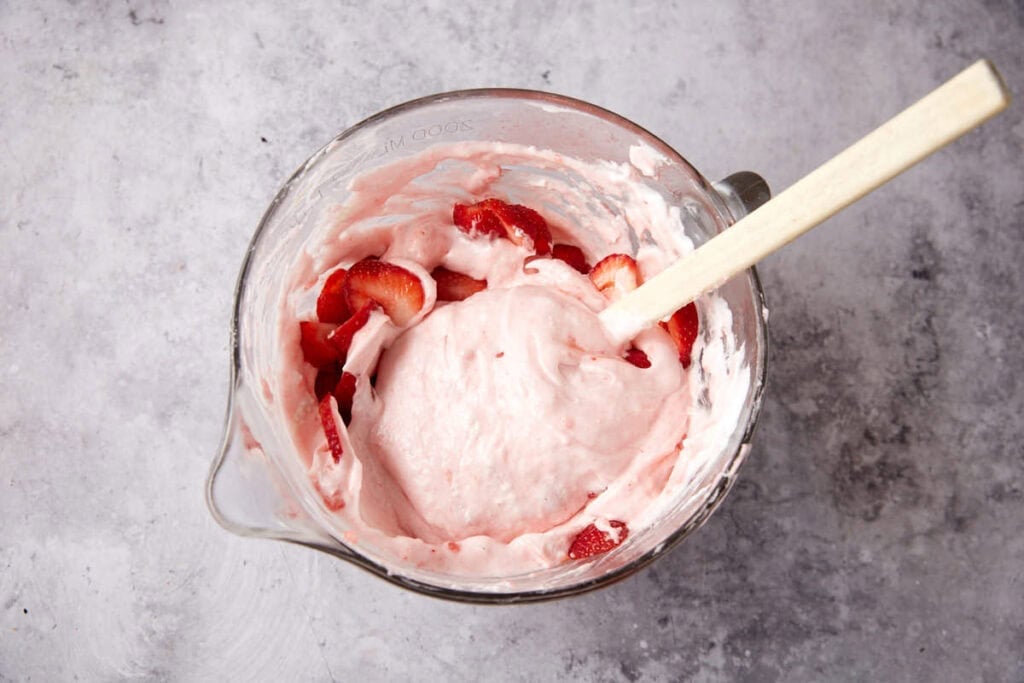 sliced strawberries being folded into the strawberry chiffon pie mixture with a spatula. 