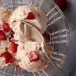 A glass bowl of strawberry ice cream with a spoon.