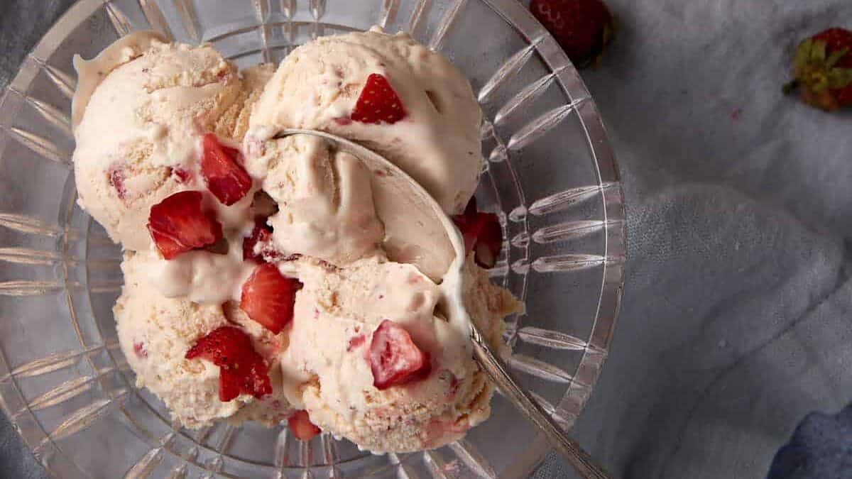 A glass bowl of strawberry ice cream with a spoon.