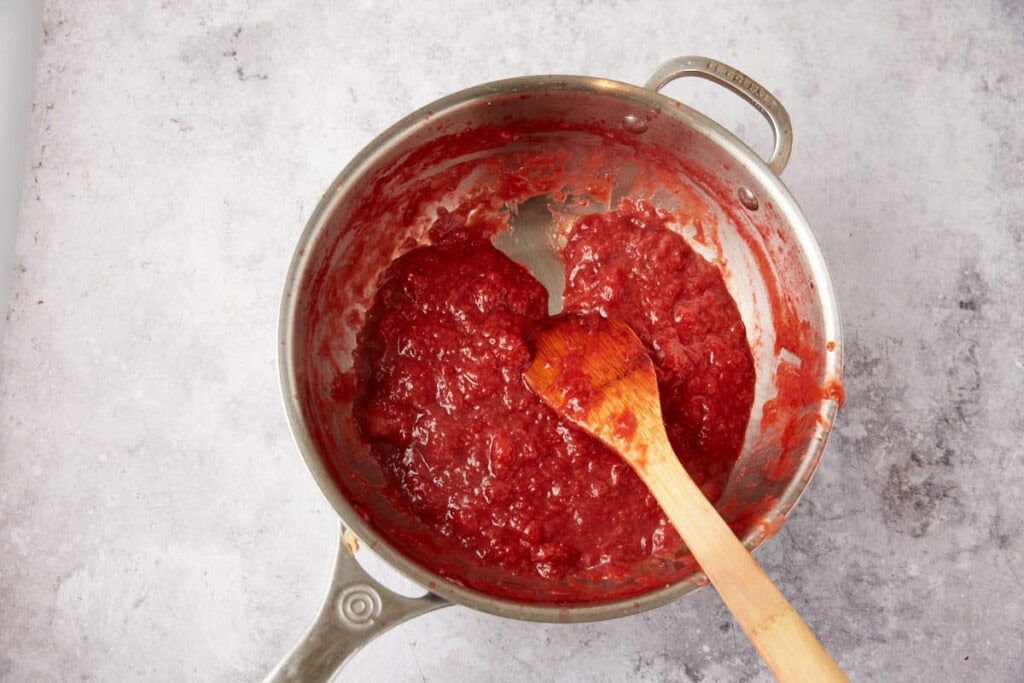A pan with strawberry sauce and a wooden spoon.