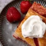 A slice of strawberry pie on a plate with whipped cream.