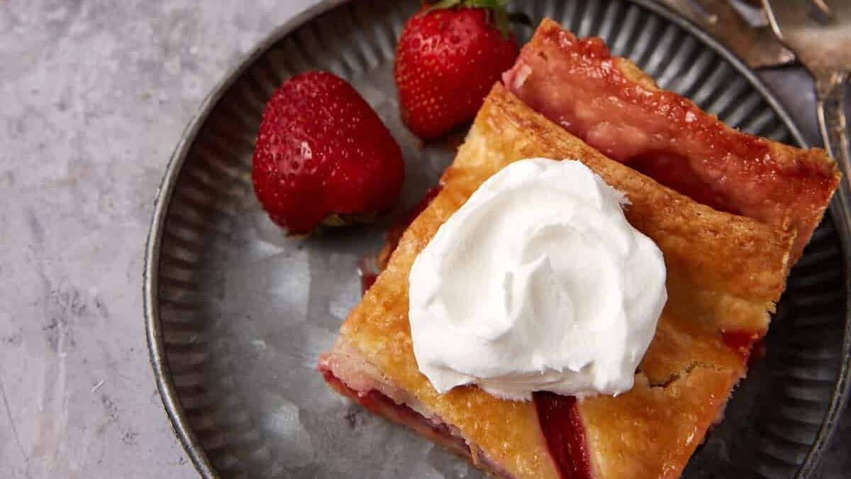 A slice of strawberry pie on a plate with whipped cream.