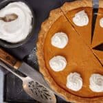 A sweet potato pie next to a bowl of whipped cream.