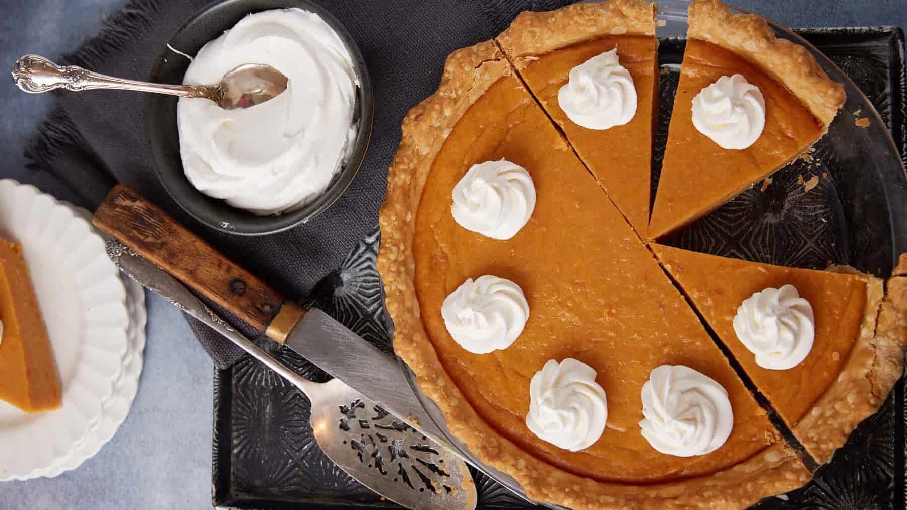 A sweet potato pie next to a bowl of whipped cream.