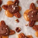 close up of pecan turtles on top of parchment paper.