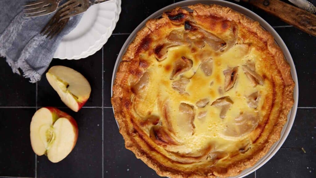 A baked apple custard pie next to some apple slices.