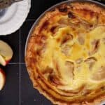A baked apple custard pie next to some apple slices.