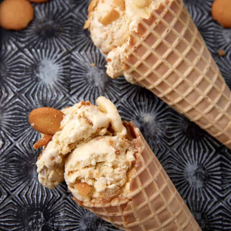 banana pudding ice cream in waffle cones with vanilla wafers in the background.