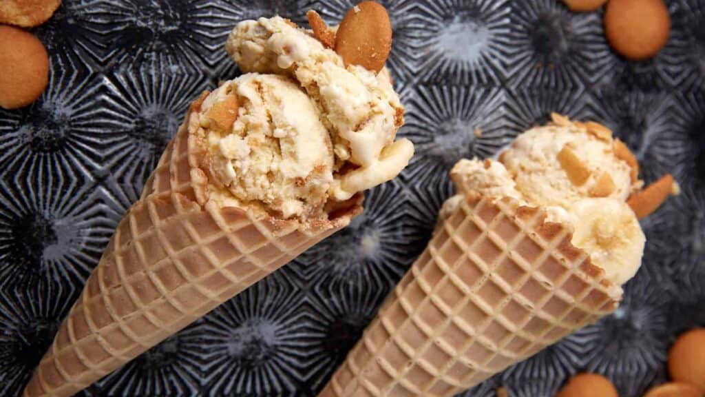 banana pudding ice cream in waffle cones with vanilla wafers in the background.