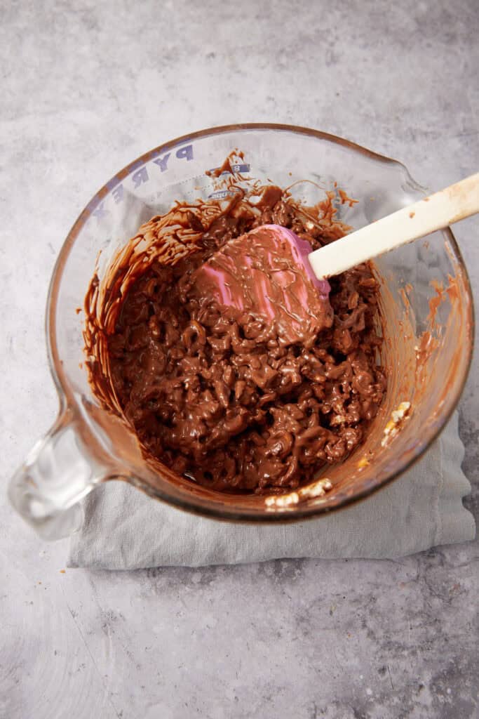 chocolate cluster mixture in a glass mixing bowl with a spatula.