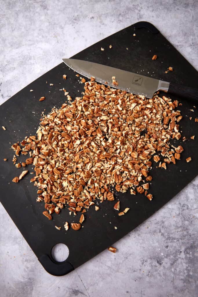 chopped pecans on a black cutting board with a knife on the side.