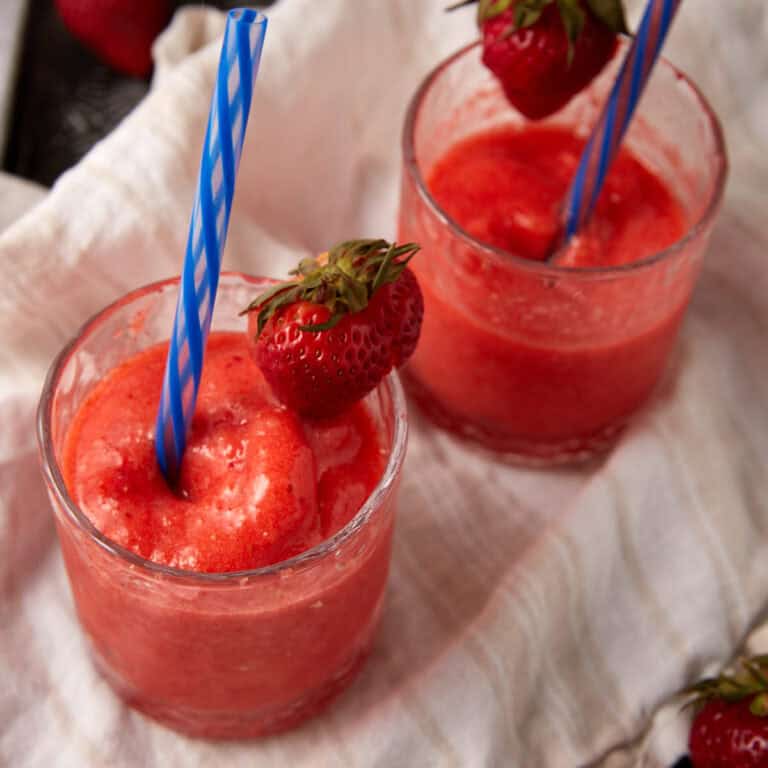 frozen strawberry lemonade in glasses with a straw and strawberry garnishes.