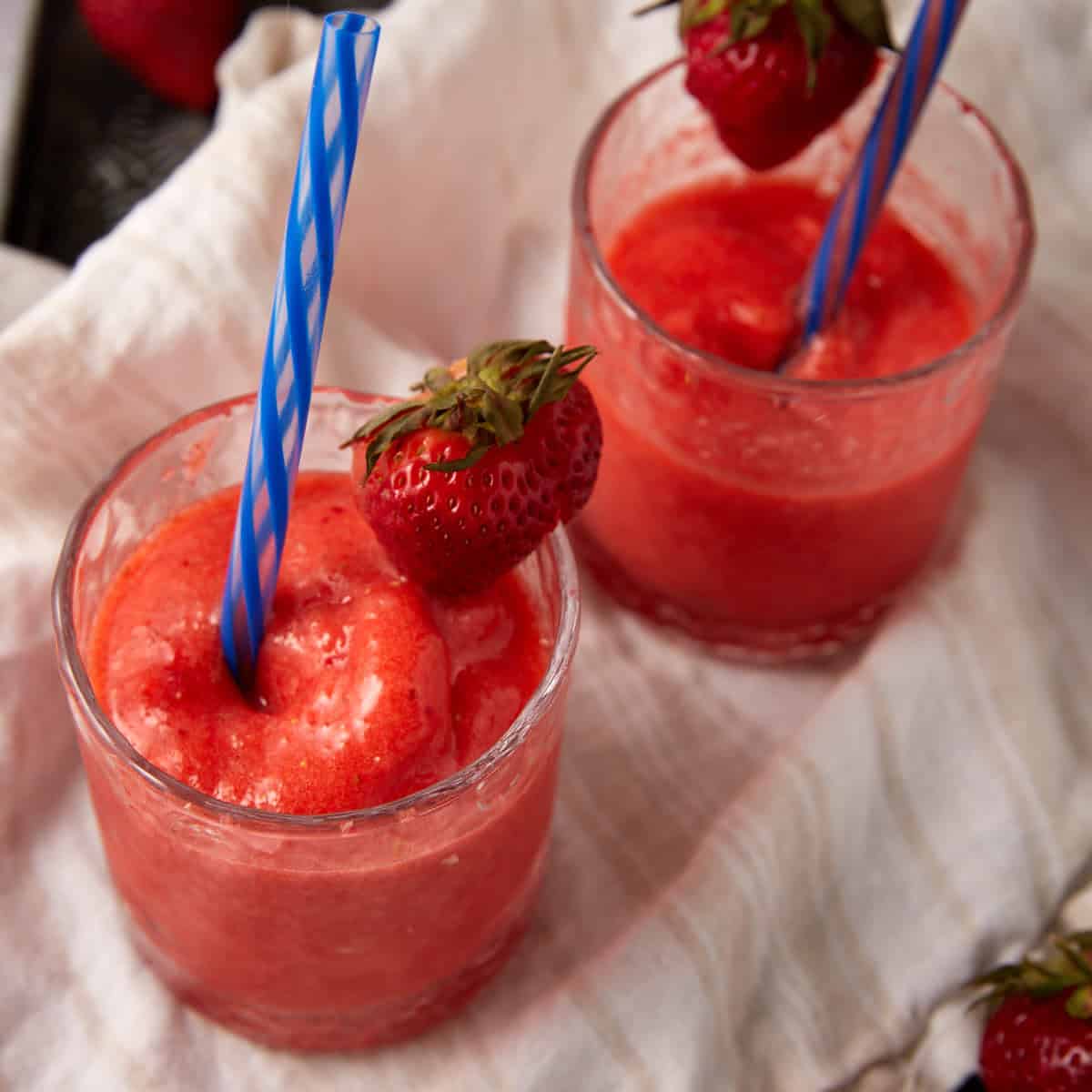 frozen strawberry lemonade in glasses with a straw and strawberry garnishes.