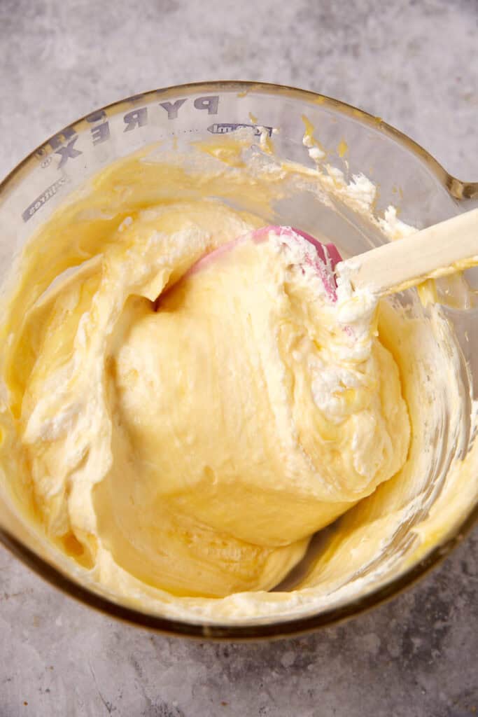 lemon curd being folded into the whipped cream in a glass bowl with a spatula.