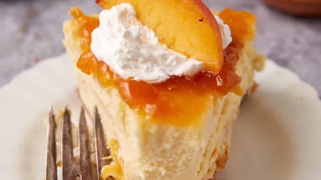slice of peach cheesecake on a white plate with a bite taken out of it.