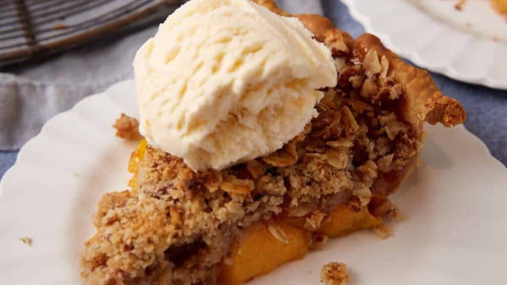 A sinlge slice of peach pie topped with vanilla ice cream.