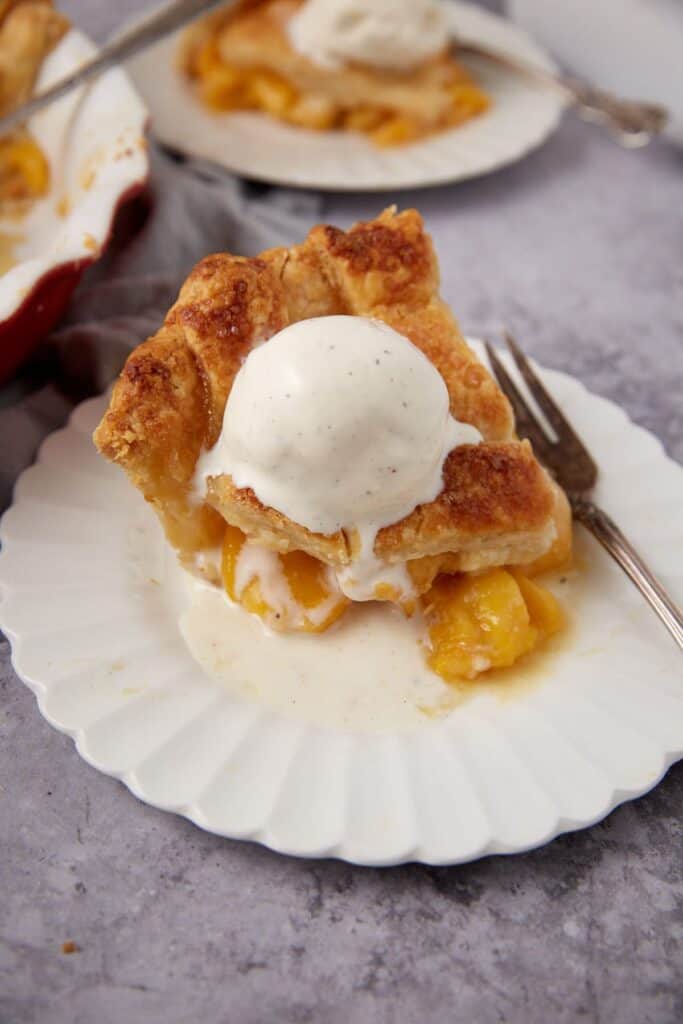 A slice of peach pie with ice cream on top.