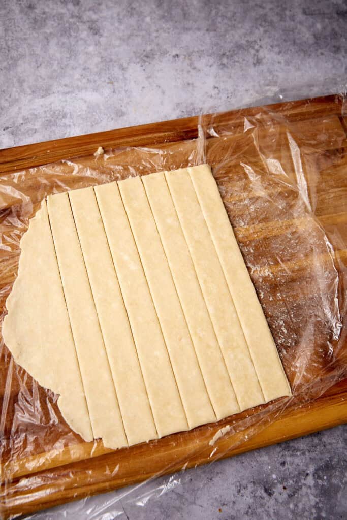 pie dough being sliced into strips on a cutting board.
