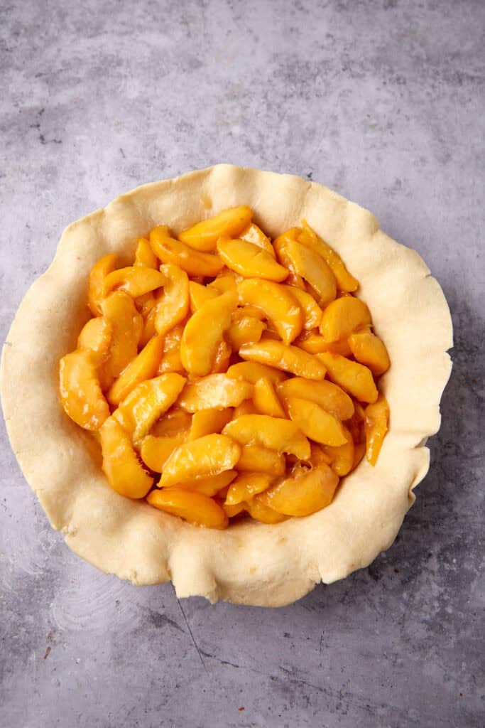 peach filling inside of a pie crust hanging over the edge of a pie dish.