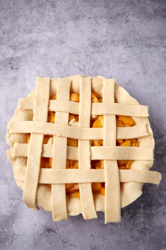 lattice crust being laid on top of a peach pie.