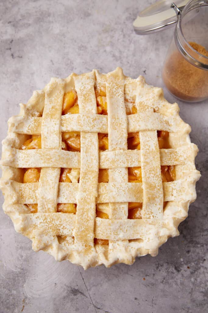 unbaked peach pie with a lattice crust coated in Demerara sugar.