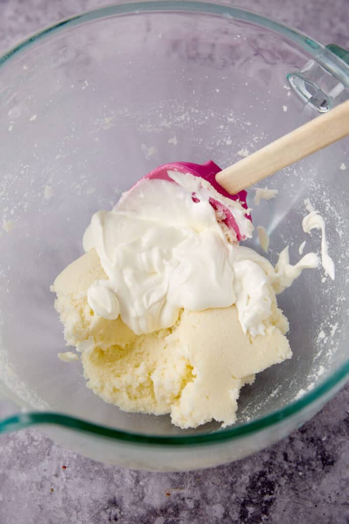 sour cream being added to beaten butter and sugar.