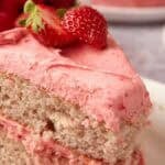 slice of strawberry cake with a bite taken out of it on a decorate plate with the strawberry cake in the background.