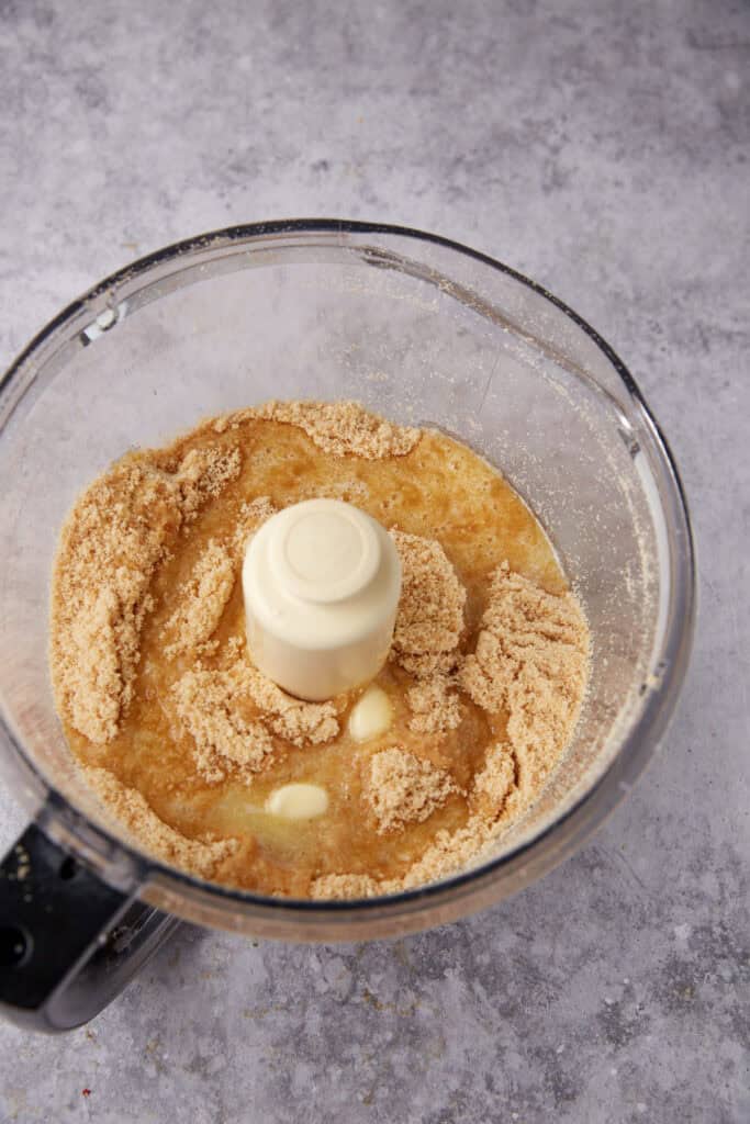 melted butter being added to crushed vanilla wafers in a food processor.
