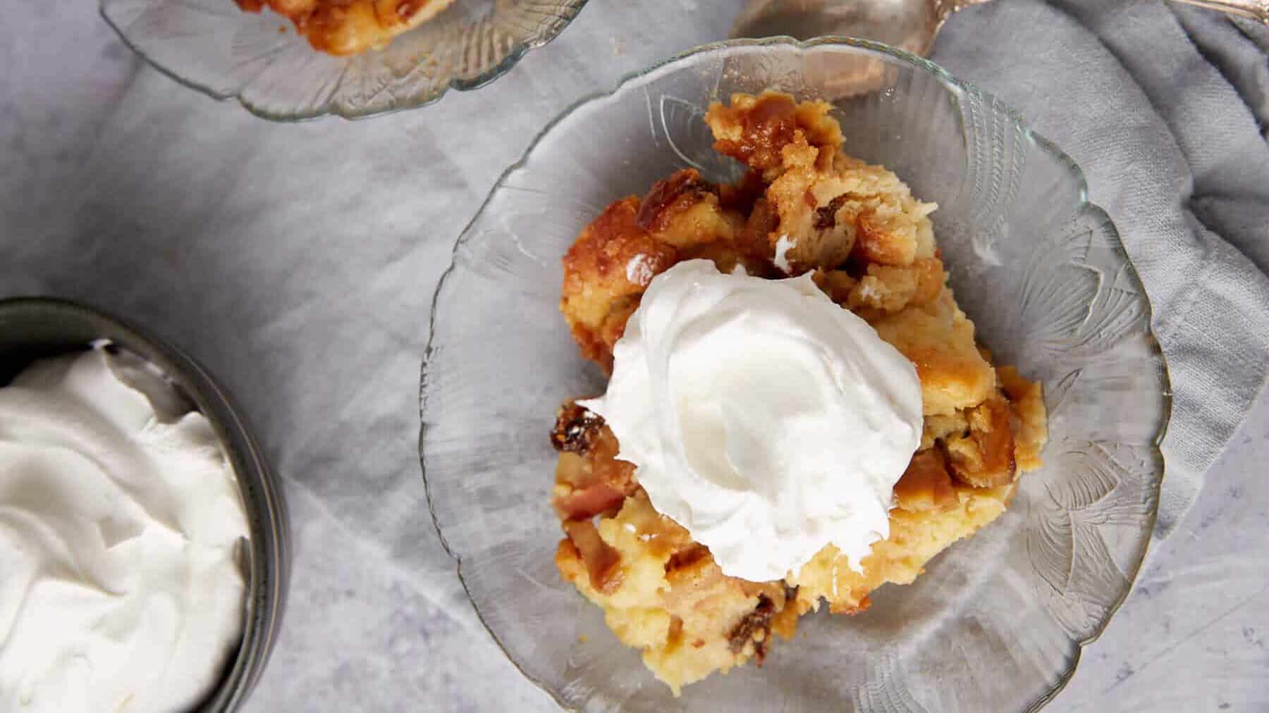 A dish of apple bread pudding topped iwth whipped cream.