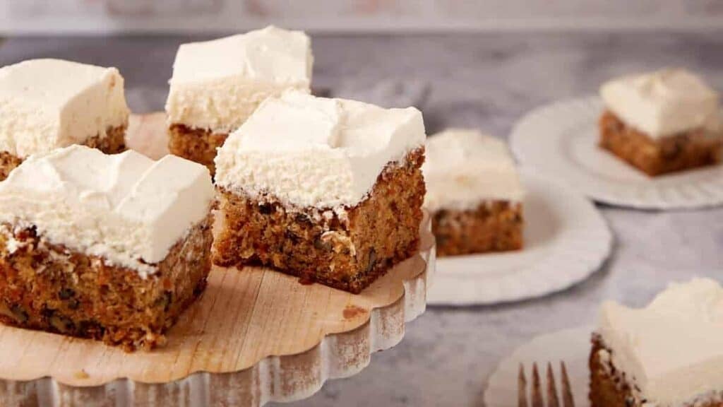 squares of carrot cake sheet cake with cream cheese frosting on a cake platter.