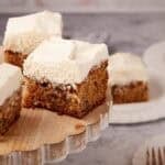 squares of carrot cake sheet cake with cream cheese frosting on a cake platter.