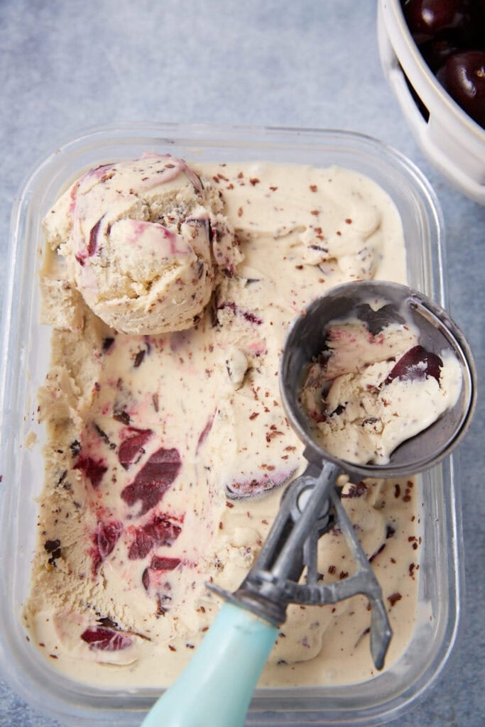 cherry chocolate ice cream in a glass dish being scooped out with an ice cream scoop.