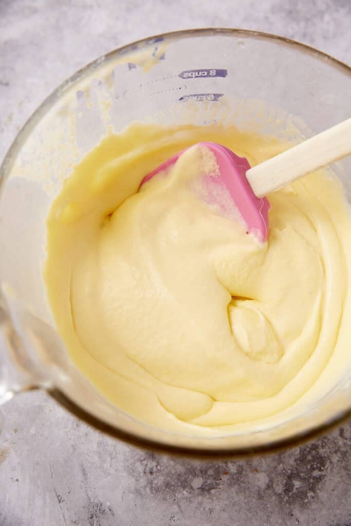 chilled custard mixture in a glass mixing bowl with a spatula.