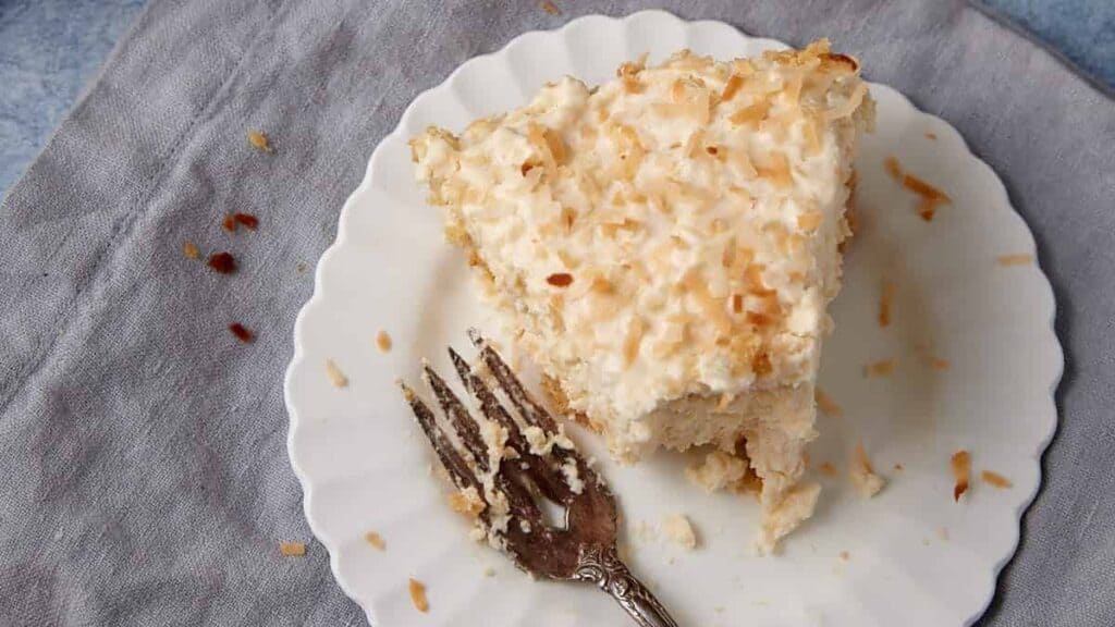 slice of coconut cream pie on a white plate with a bite taken out of it.