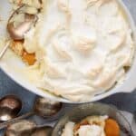 Banana pudding topped with meringue in a baking dish with a serving spoon.
