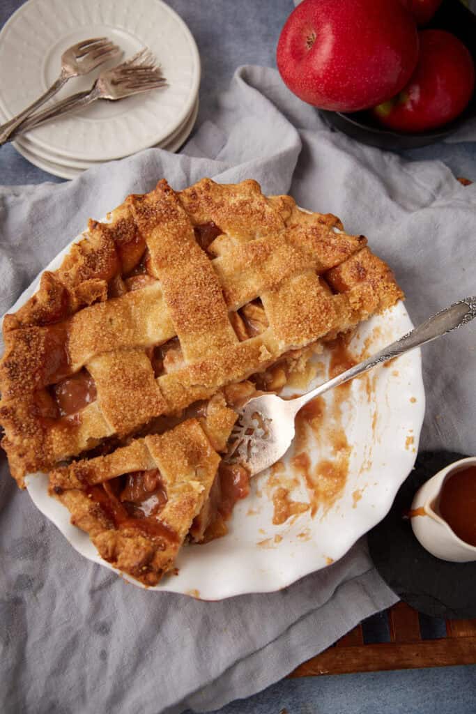 caramel apple pie in a white pie dish with two pieces taken out of it.