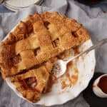 caramel apple pie in a white pie dish with two pieces taken out of it.