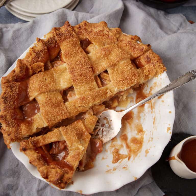 caramel apple pie in a white pie dish with two pieces taken out of it.