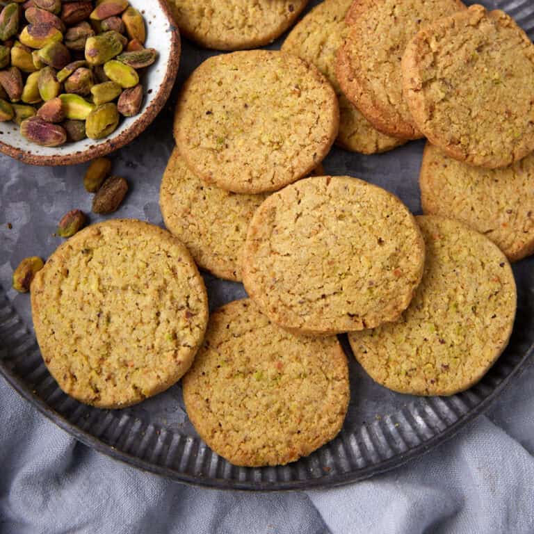 A tray filled with golden pistachio shortbread cookies and a small bowl of pistachios.