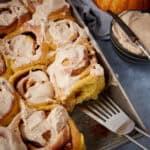 iced pumpkin cinnamon rolls in a baking dish with a spatula.