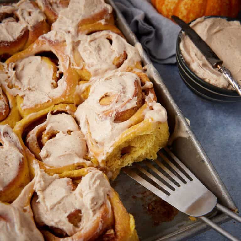 iced pumpkin cinnamon rolls in a baking dish with a spatula.