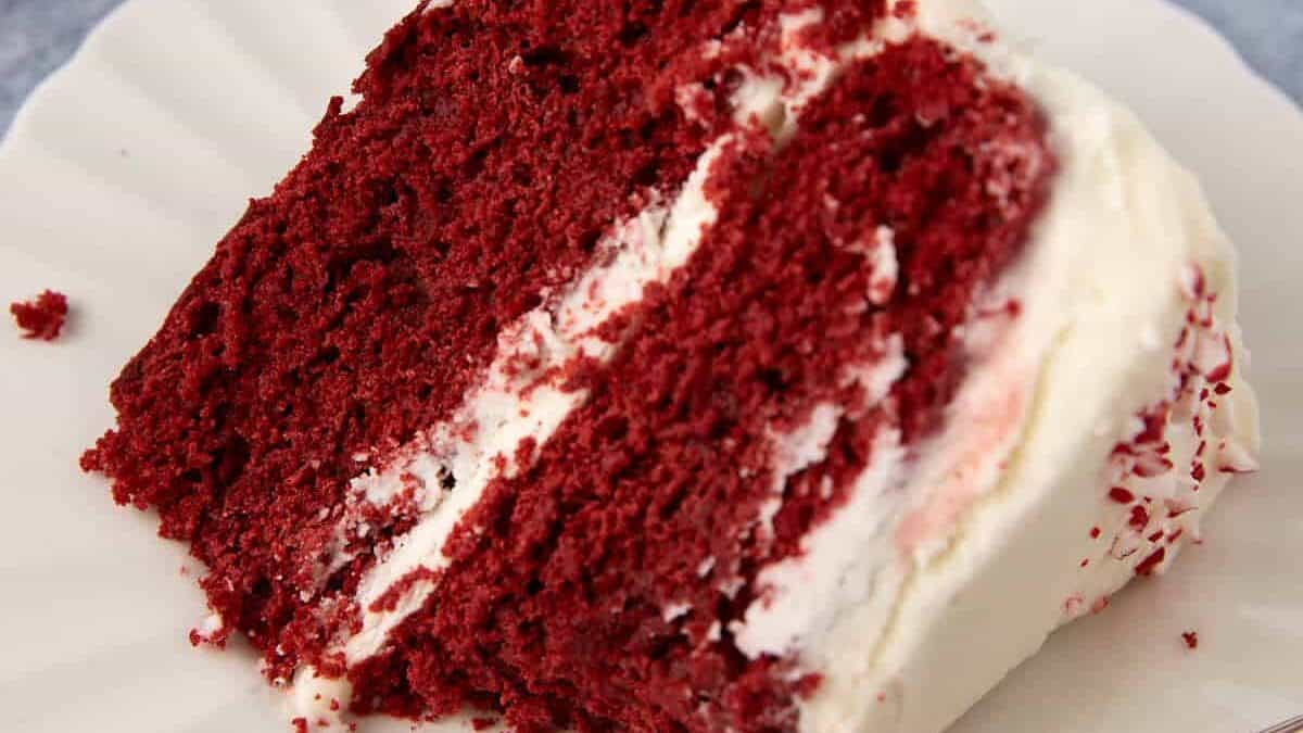A slice of red velvet layer cake with a bite taken out.