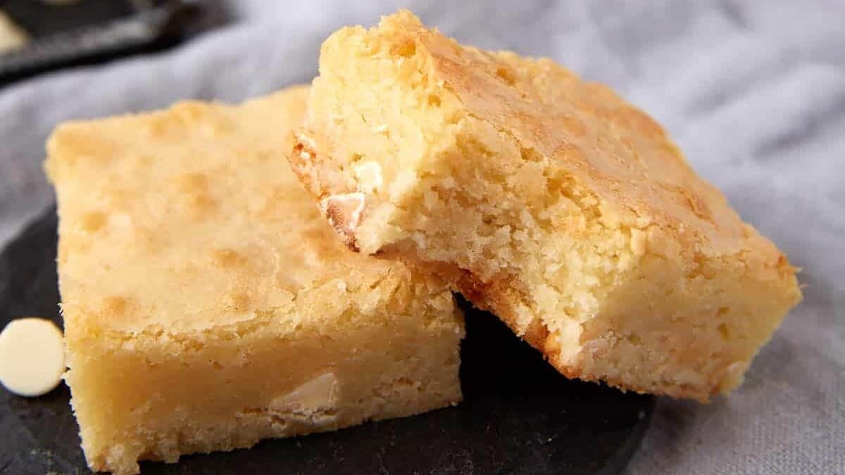 white chocolate brownies with a bite taken out of one on a black plate.
