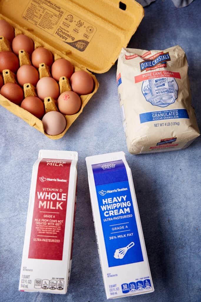 Carton of brown eggs, a bag of granulated sugar, and cartons of whole milk and heavy whipping cream arranged together, showing key ingredients for ice cream.