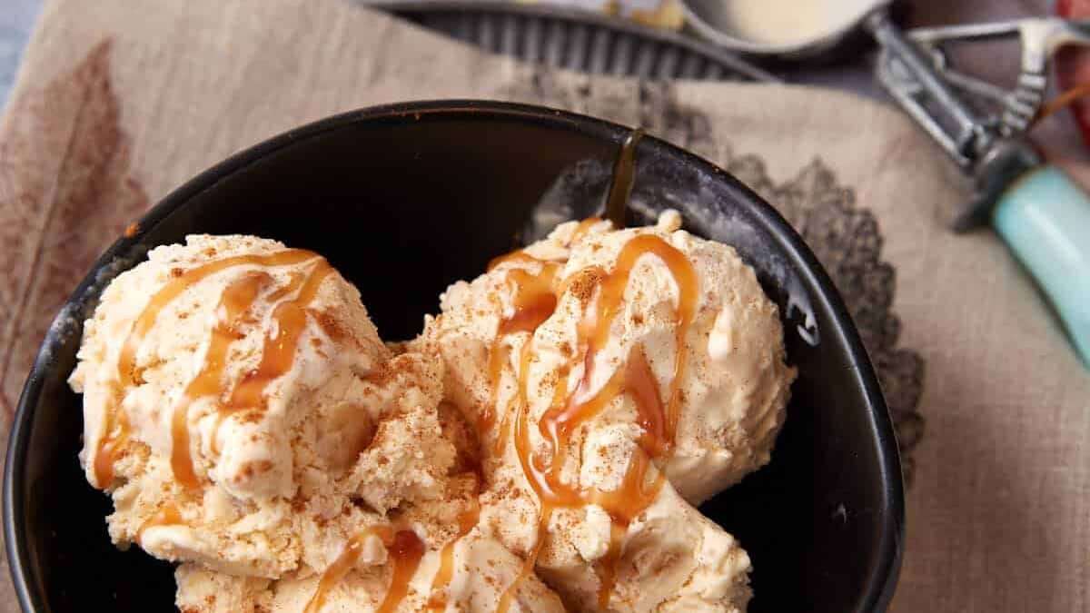 Overhead view of apple crisp ice cream scooped into a black bowl, set on a tan linen with ice cream