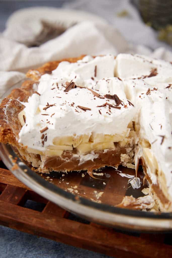 A partially sliced Banoffee Pie in a glass pie dish, showing visible layers of banana and caramel.